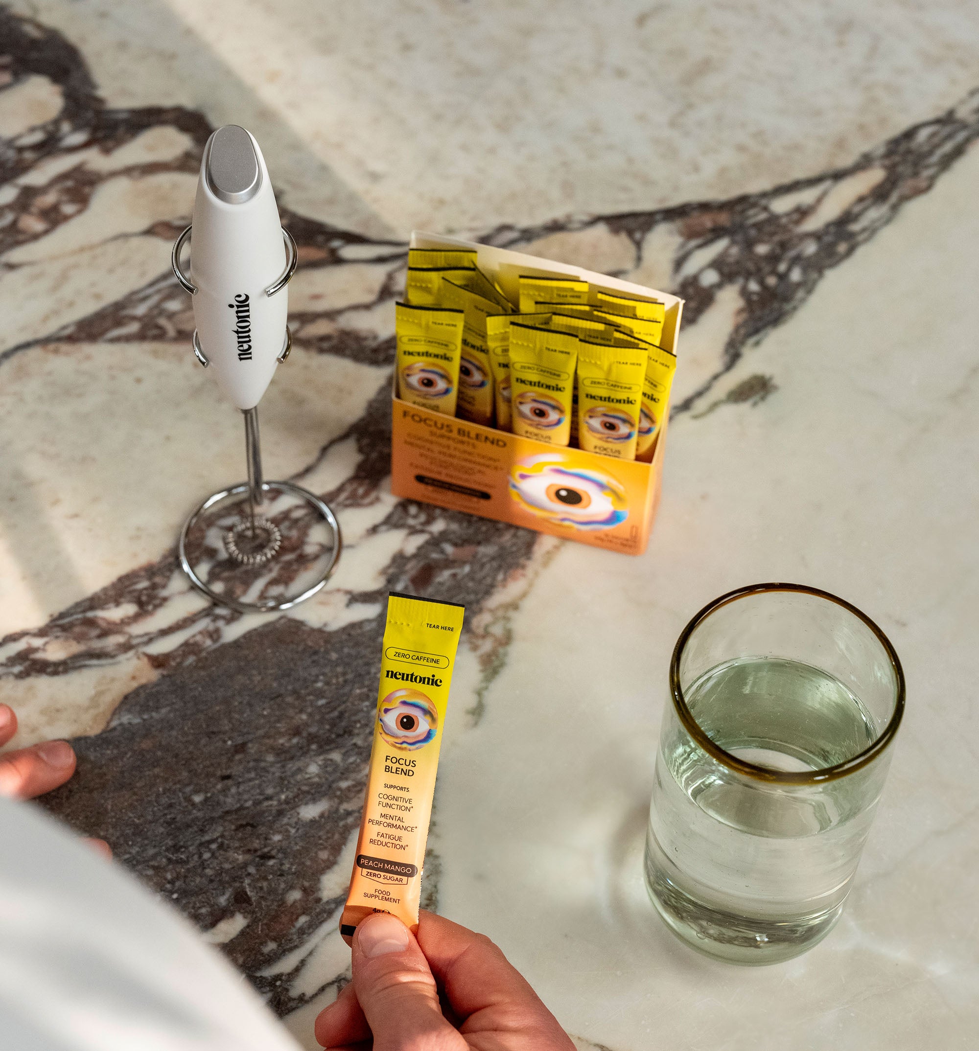 White handheld whisk with stainless steel head beside nootropics sachets and a glass of water on marble surface. - Neutonic - Handheld Whisk