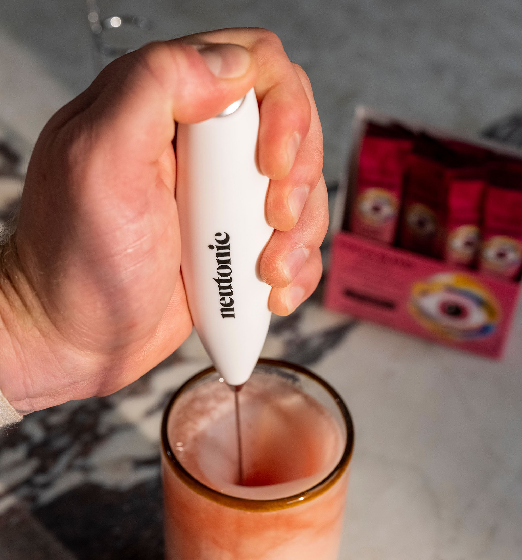 White handheld whisk labeled neurotific blending a drink, with nootropics supplement packets in the background. - Neutonic - Handheld Whisk